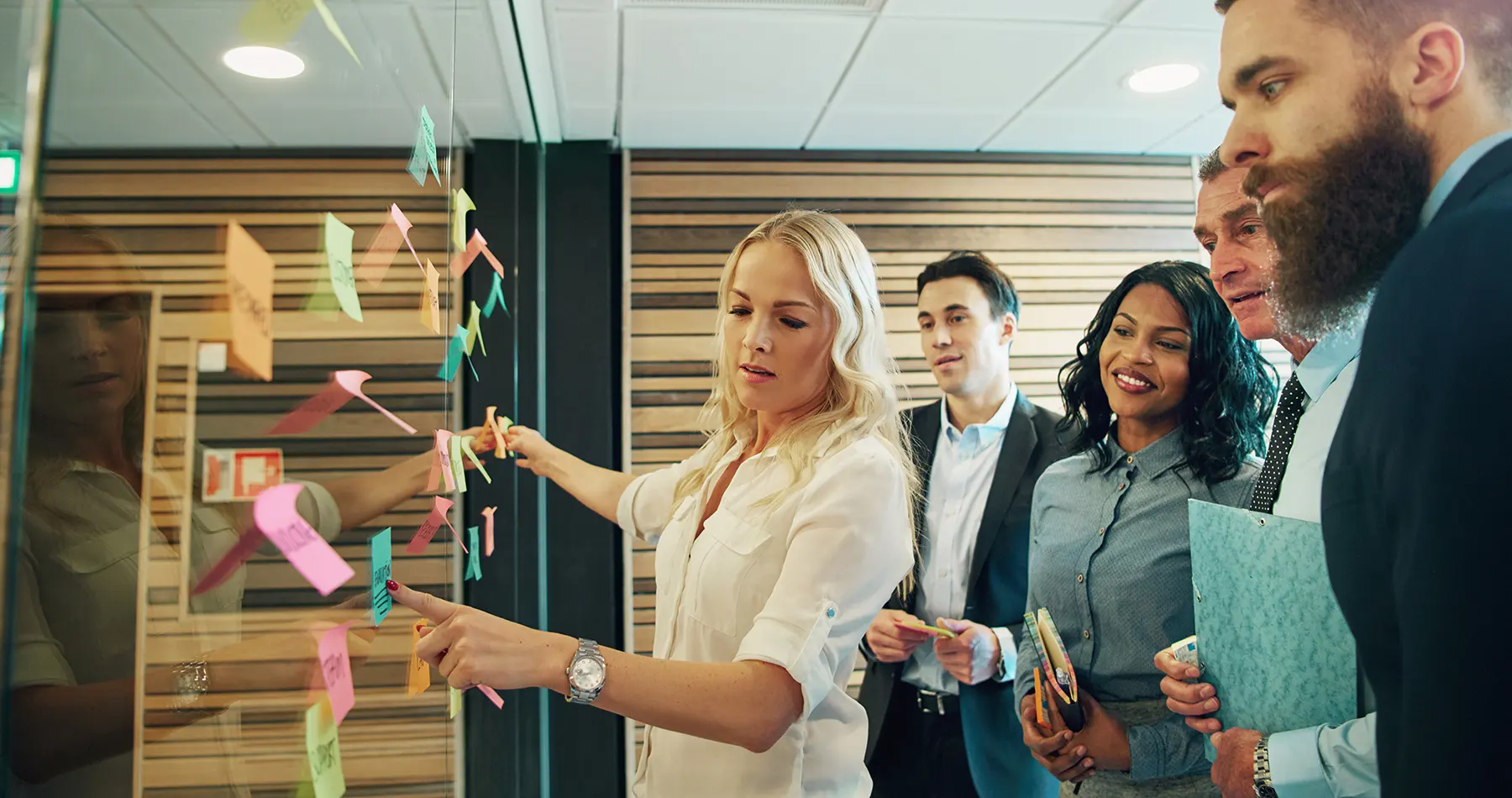 people standing around a white board while a female points to a post it note.